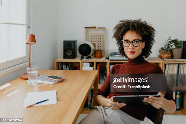 successful young afro woman sitting at her desk in her home office - maroon stock pictures, royalty-free photos & images