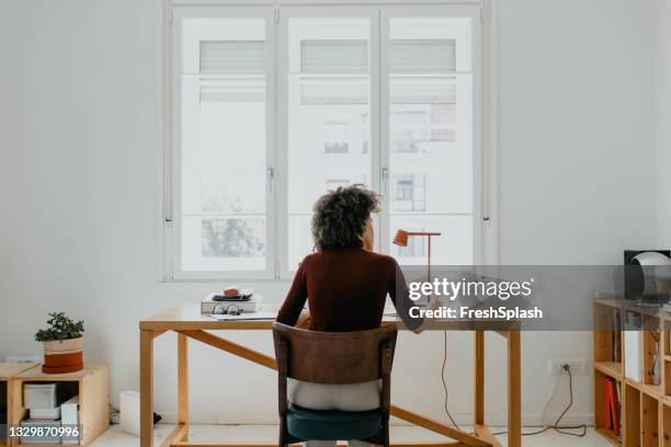unrecognizable successful young afro woman sitting at her desk in her home office - sunny office stock pictures, royalty-free photos & images