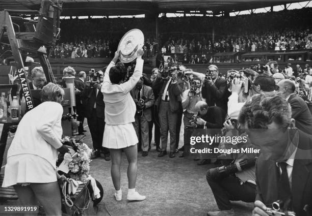 Press photographers gather around as Billie Jean King of the United States holds the Venus Rosewater Dish aloft after defeating Ann Jones of Great...