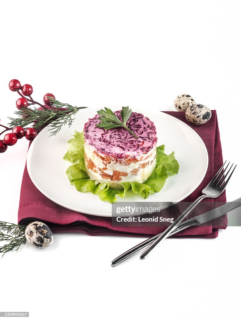 Food photography of classic Russian New Year salad "Shuba" side view with mayonnaise, salted herring or salmon, boiled vegetables (beetroot, carrot) on a white background isolated close up