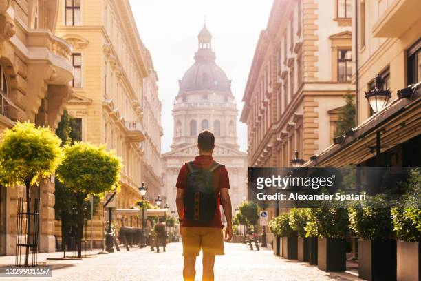 rear view of a young man with backpack exploring the streets of budapest, hungary - budapest foto e immagini stock