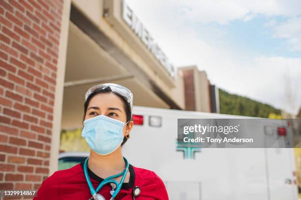 young woman medical professional standing outside emergency room of hospital wearing mask - person in emergency hospital stockfoto's en -beelden