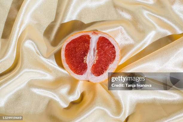 fresh grapefruit on beige soft silk fabric background. sex concept. women's health, sexuality, erotic tension. female vagina and clitoris symbol. - scheide stock-fotos und bilder