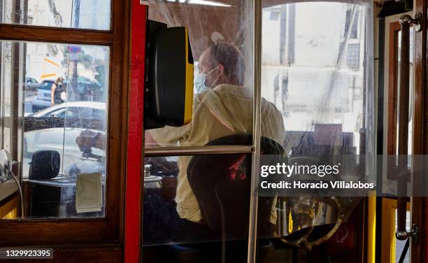 Mask-clad 24 Line tram driver is seen through thick plastic protection during the COVID-19 Coronavirus pandemic on July 21, 2021 in Lisbon, Portugal....