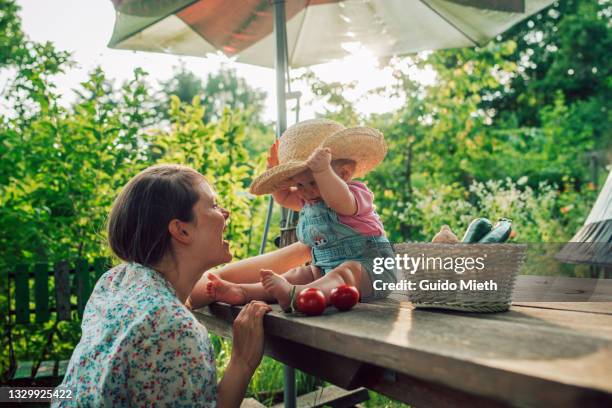 cheerful mother and daughter having fun while baby trying mothers hat. - beautiful baby stockfoto's en -beelden