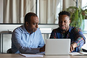 Two African American employees working on project together, using laptop