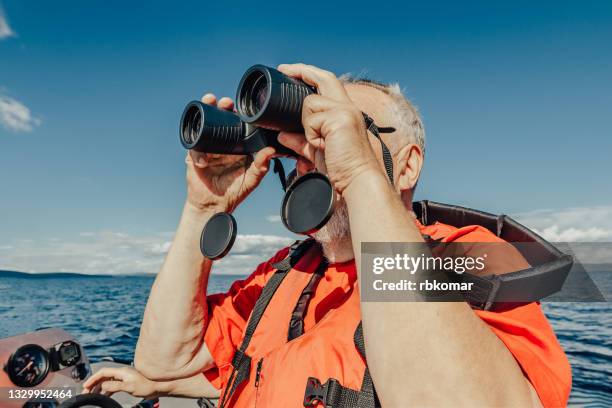 old man sailor in life jacket watching the sea through binoculars - binoculars isolated stock pictures, royalty-free photos & images