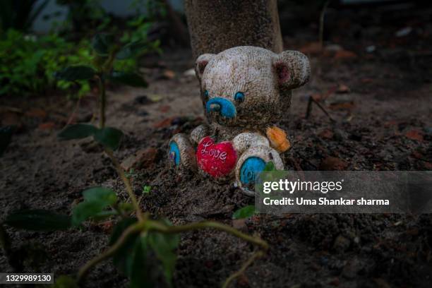 rotten teddy bear. toy bear holding a  heart all caught up in dirt and mud thrown out side in the backyard. - unwanted present stock pictures, royalty-free photos & images