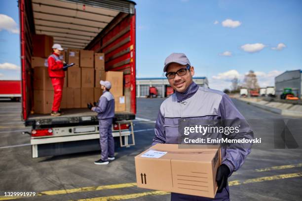 happy delivery man with cardboard box looking at camera - lossen stockfoto's en -beelden