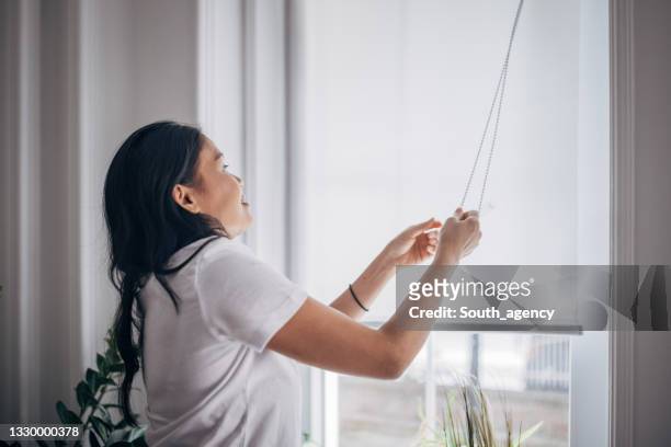 woman lowering blinds on window - lower stockfoto's en -beelden