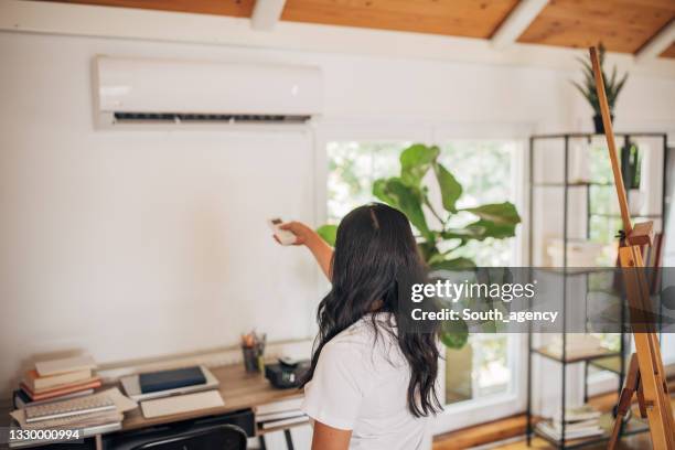 woman turning on air conditioner - ac stockfoto's en -beelden