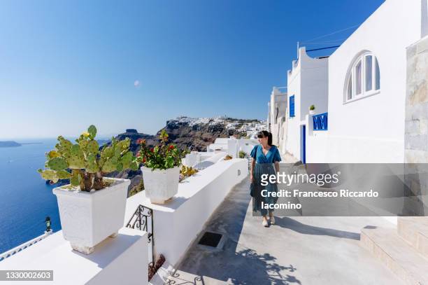 fira, santorini island, cyclades, greece. houses and churches, white houses and stairs. woman tourist dressed in blue - luxury location stock-fotos und bilder
