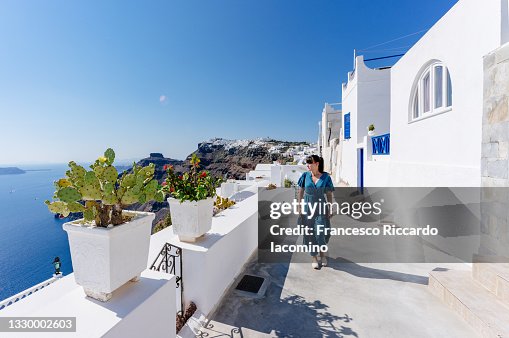Fira, Santorini Island, Cyclades, Greece. Houses and churches, white houses and stairs. Woman tourist dressed in blue Fira, Santorini Island, Cyclades, Greece. Houses and churches, white houses and stairs. Woman tourist dressed in blue
