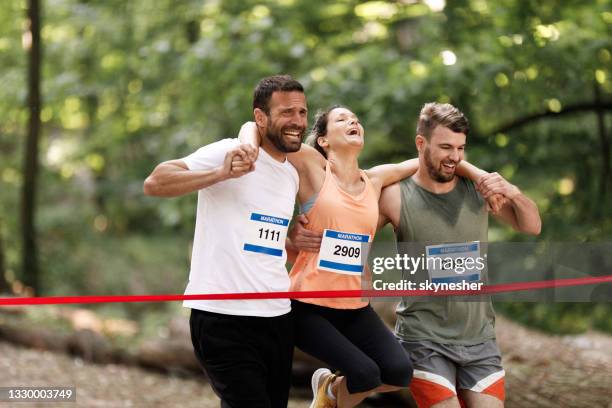 two athletic men carrying their injured friend while crossing the finish line together. - injured runner stock pictures, royalty-free photos & images