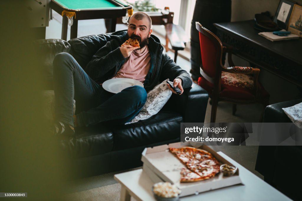 Man watching TV and eating take-out pizza at home