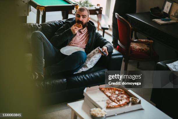 man watching tv and eating take-out pizza at home - atividade imóvel imagens e fotografias de stock