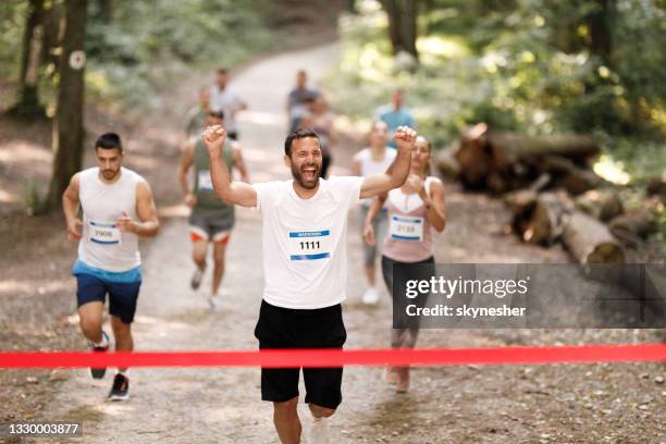 erfolgreicher marathonläufer überquert mit erhobenen armen die ziellinie. - marathon ziel stock-fotos und bilder