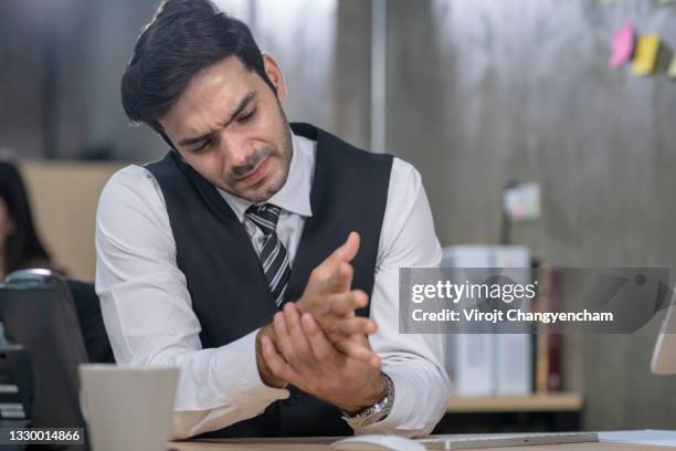 business man holds wrist in pain while working in the office - hold wrists imagens e fotografias de stock