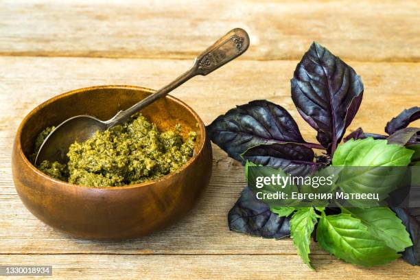 homemade pesto alla genovese sauce in bamdoo bowl with spoon and basil leaves on wooden background - pesto stock-fotos und bilder