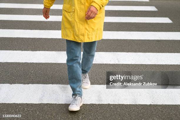 a young woman walks alone through a pedestrian crossing. the feet of a girl in jeans and sneakers step on a white zebra stripe, close-up. the concept of safety, proper lifestyle, compliance with traffic rules. - zebra crossing stock-fotos und bilder