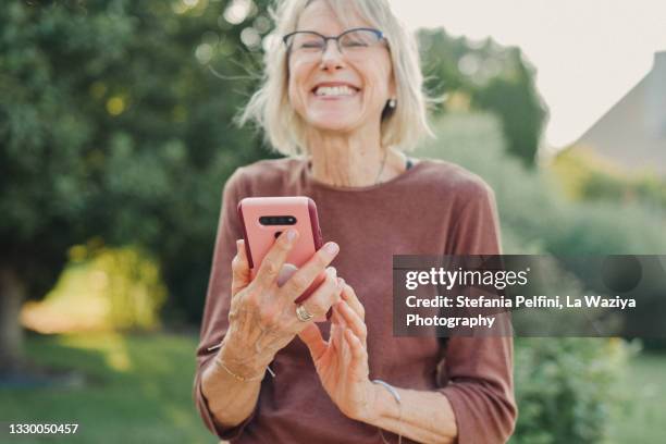 senior woman smiling while using her smartphone - woman smartphone nature stockfoto's en -beelden