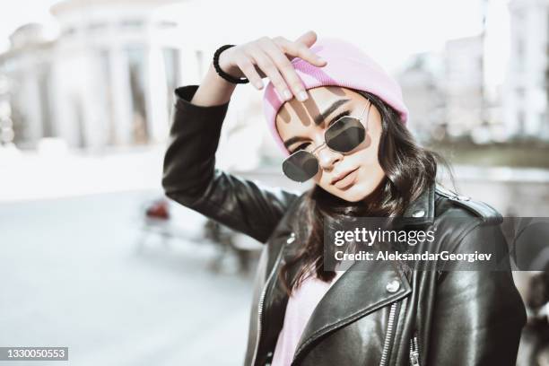 cute female portrait wearing pink knit hat and leather jacket while shielding from sunlight - gothic style stockfoto's en -beelden