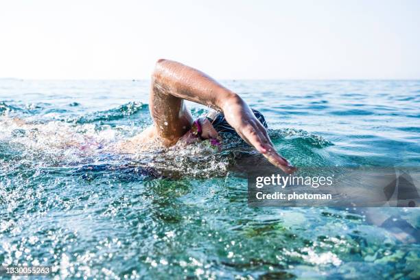 menschlicher körperarm teil eines schwimmers, der im blauen meer trainiert - schwimmwettkampf stock-fotos und bilder