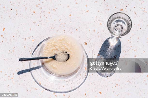 chicken soup in a transparent dish and glass of water with shadows and pasta outside - terrazzo ストックフォトと画像