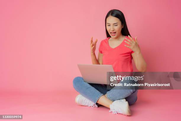 full length bad expression asian woman in red clothes and casual jean sitting on floor using laptop  mock up in hand isolated on pink background with copy space - fabulous full lengths foto e immagini stock