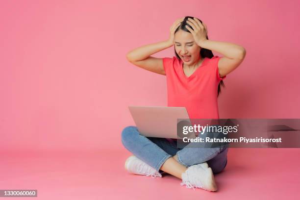 full length bad expression asian woman in red clothes and casual jean sitting on floor using laptop  mock up in hand isolated on pink background with copy space - fabulous full lengths foto e immagini stock