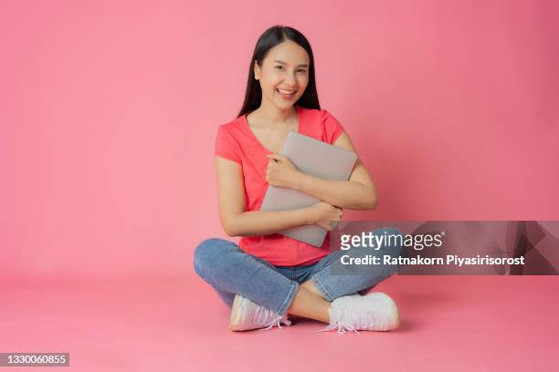 full length good expression asian woman in red clothes and casual jean sitting on floor holding laptop mock up in hand isolated on pink background with copy space - fabulous full lengths foto e immagini stock