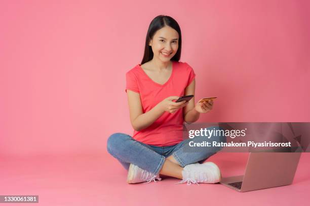 full length good expression asian woman in red clothes and casual jean sitting on floor with laptop mock up holding credit card and smartphone mockup in hand isolated on pink background with copy space, shopping online concept - fabulous full lengths foto e immagini stock