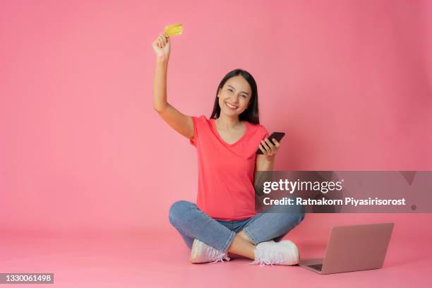 full length good expression asian woman in red clothes and casual jean sitting on floor holding laptop mock up showing credit card mockup in hand isolated on pink background with copy space, shopping online concept - fabulous full lengths foto e immagini stock