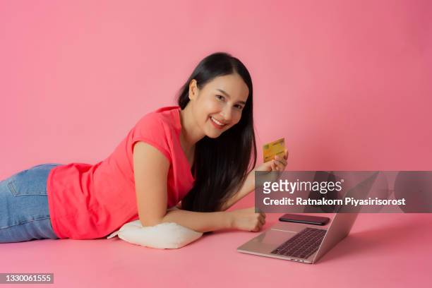 full length good expression asian woman in red clothes and casual jean lying on floor holding laptop mock up showing credit card mockup in hand isolated on pink background with copy space, shopping online concept - fabulous full lengths foto e immagini stock