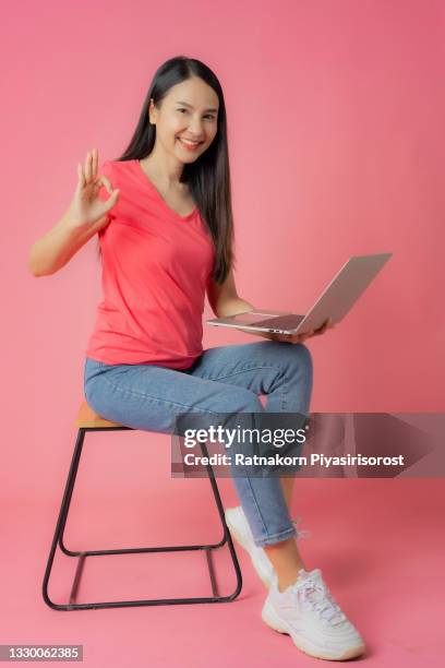 full length good expression asian woman in red clothes and casual jean sitting on floor using laptop  mock up in hand isolated on pink background with copy space - fabulous full lengths foto e immagini stock