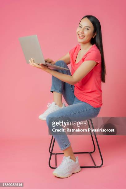 full length good expression asian woman in red clothes and casual jean sitting on floor using laptop  mock up in hand isolated on pink background with copy space - fabulous full lengths foto e immagini stock