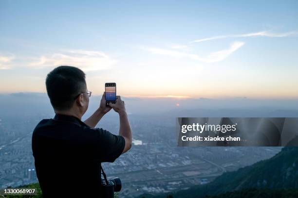 male tourist using mobile phone to take photos on top of the mountain - fuzhou stock pictures, royalty-free photos & images