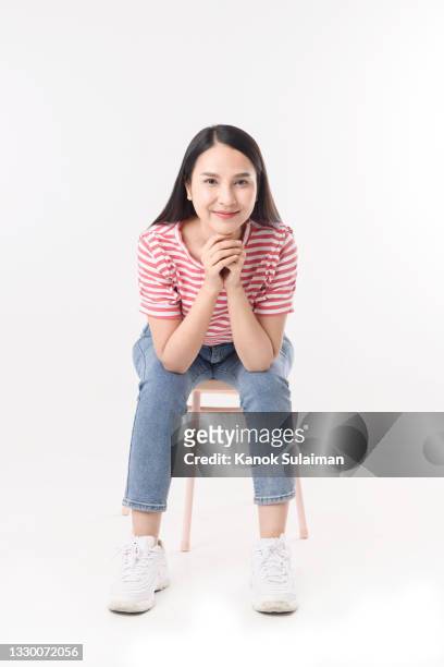 portrait of smiling woman sitting on chair with white background - woman wearing white jeans ストックフォトと画像