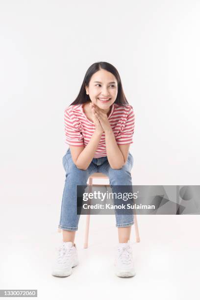 portrait of smiling woman sitting on chair with white background - woman excited sitting chair stock pictures, royalty-free photos & images