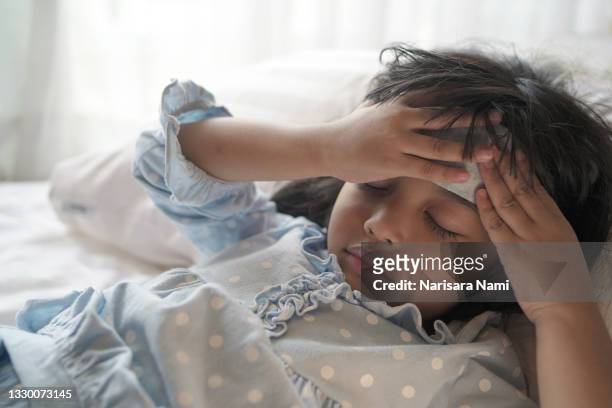 asian patient kid in the hospital is having a medical treatment after received a virus. and having a cooling fever patch on the forehead. - headache child fotografías e imágenes de stock