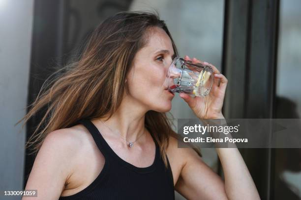 portrait of young woman in black dress drinking water with lemon - thirsty stock pictures, royalty-free photos & images