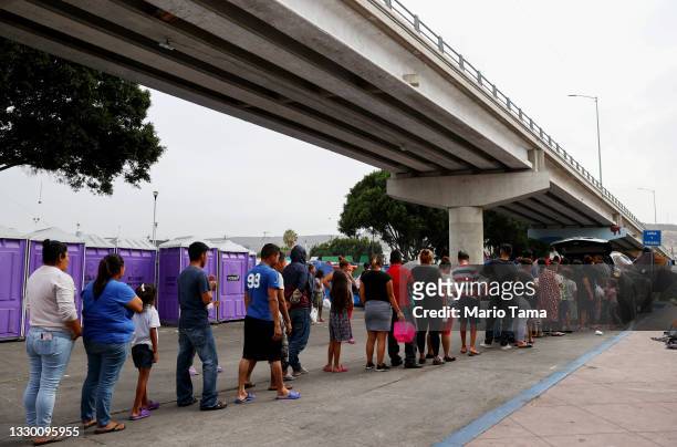 Asylum-seeking migrants wait in line for donated food at a makeshift migrant camp on the Mexican side of the San Ysidro Port of Entry on July 22,...