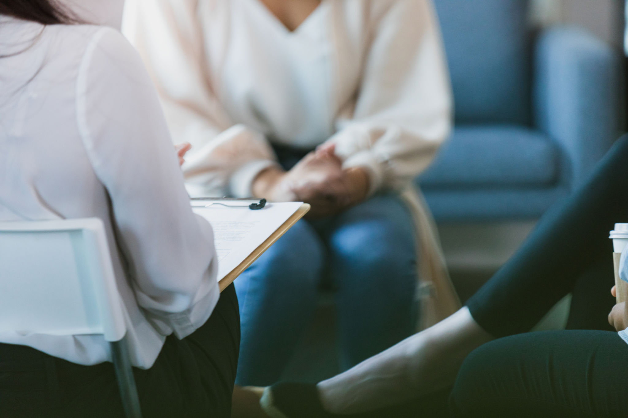 Women in group therapy listen to unrecognizable therapist with clipboard Women in group therapy listen to unrecognizable therapist with clipboard