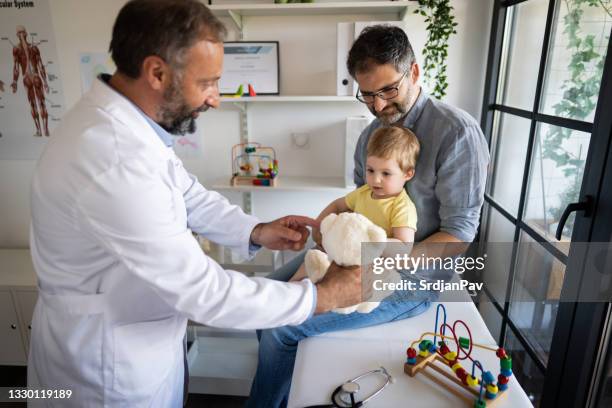 cheerful mature male pediatrician giving a baby boy teddy bear to play with - baby stuffed animal bildbanksfoton och bilder