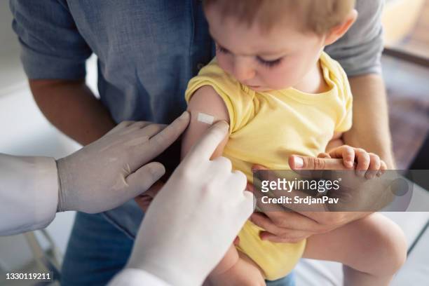 un médico irreconocible colocando un parche en el hombro del niño después de una vacunación exitosa - vacuna fotografías e imágenes de stock