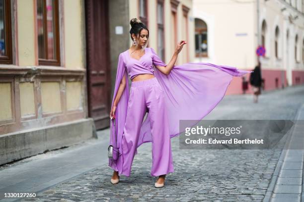 Isabela Francesca wears bejeweled earrings, a pastel purple low-neck cropped top with oversized long flared flowing sleeves, matching pastel purple...