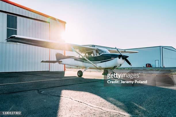 sonnenaufgangsaufnahme eines kleinen einmotorigen flugzeugs im freien vor einem hangar - airplane hangar stock-fotos und bilder