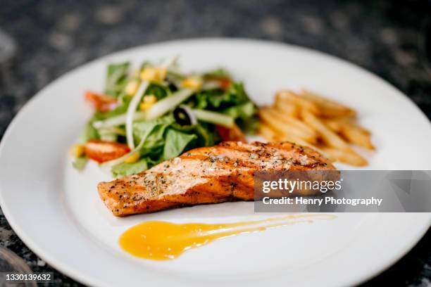 a white plate of the pan seared salmon fillet with lemon butter sauce - zalm stockfoto's en -beelden