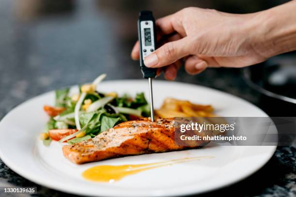 chef uses a thermometer to measure the temperature of the pan seared salmon fillet - meat stock pictures, royalty-free photos & images