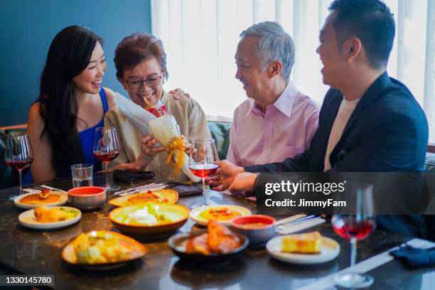 happy asian mum receiving a bouquet of flowers from her family at the dining table. - asian couple dinner stock pictures, royalty-free photos & images